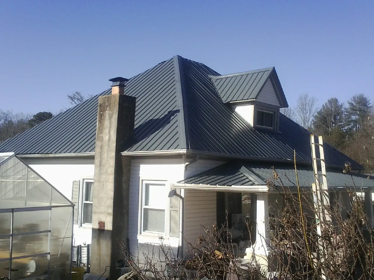 Dark blue standing seam metal roof on a white farmhouse with dormer — Slate & Tile Roof Repair by Roofing Brothers in Boyd