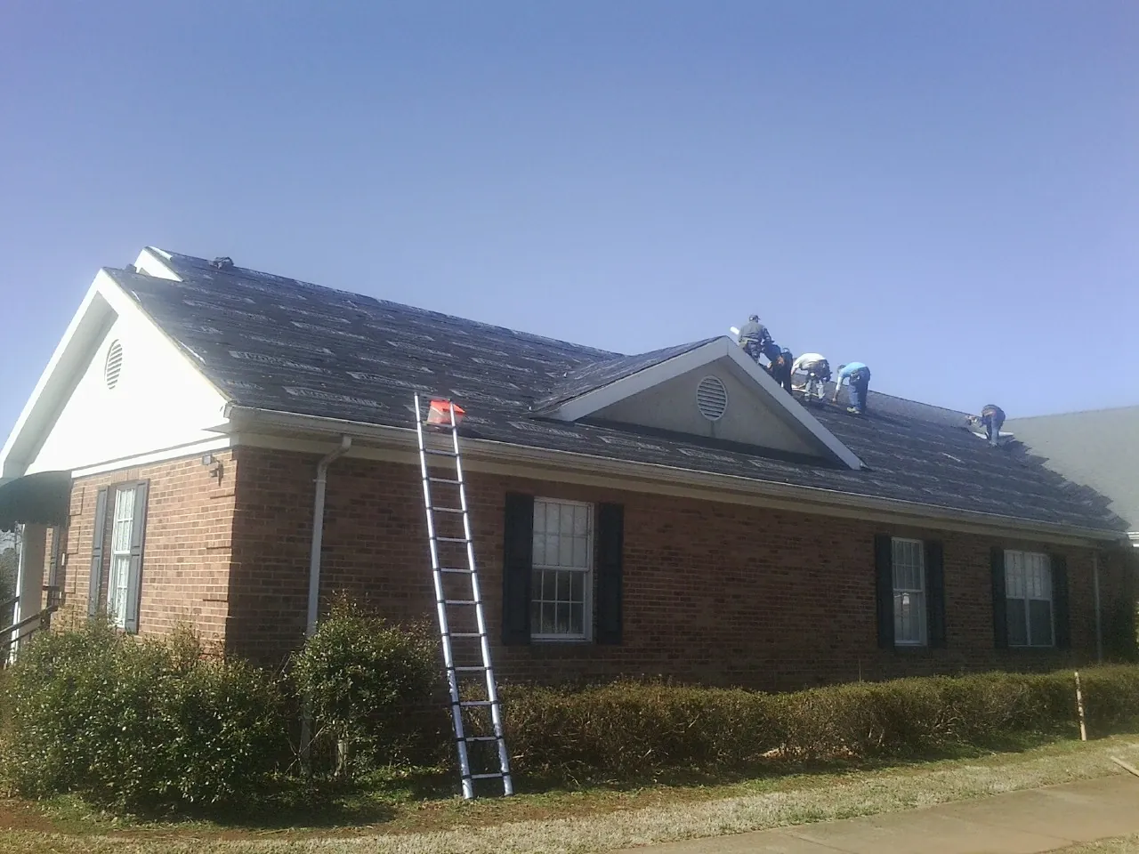 Crew tearing shingles off a brick ranch roof with a ladder set — Metal Roof Repair work by our crew in Boyd