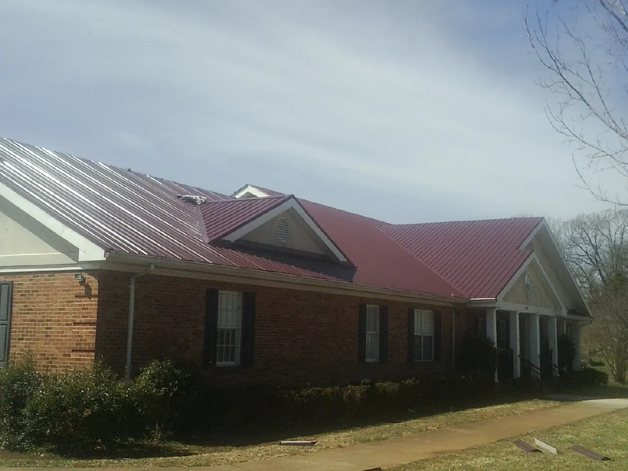 Red metal roof with gabled entries on a long brick building, from a Hail Damage Roof Repair job in Boyd
