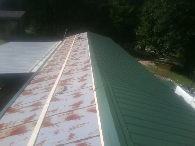 Old rusted panels beside newly installed green metal roofing — Wind Damage Roof Repair by Roofing Brothers in Boyd