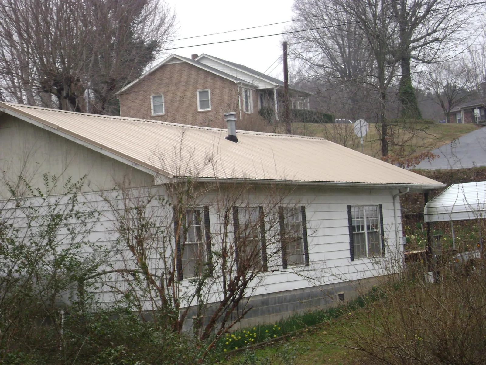 Tan metal roof on a white sided house set into a hillside — Commercial Roofing by Roofing Brothers in Boyd