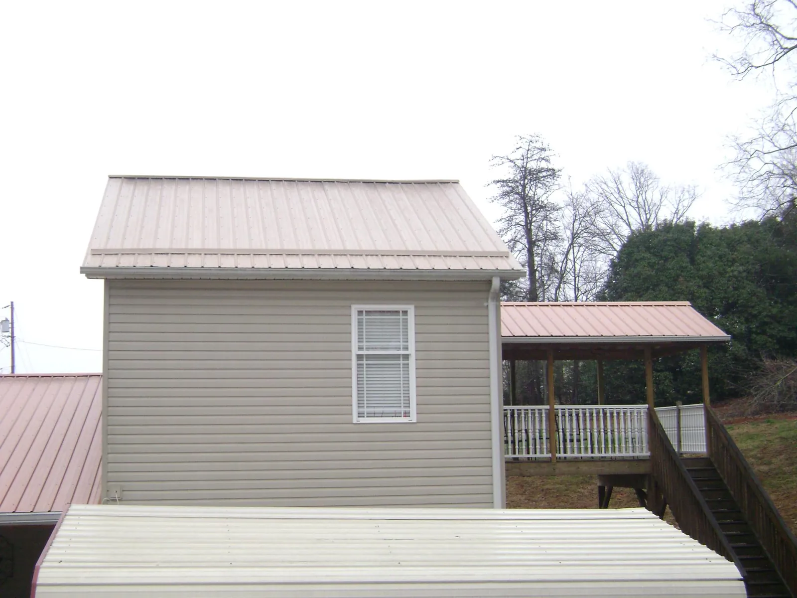 Tan metal roofs on a two story addition and attached porch, from a Roof Replacement job in Boyd